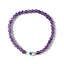 Purple beaded bracelet with a gold and silver evil eye charm on a white background