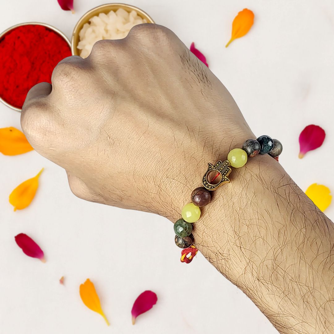 Hand wearing a beaded rakhi with colorful stones, surrounded by flower petals on a light background.