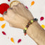 Hand wearing a beaded rakhi with colorful stones, surrounded by flower petals on a light background.