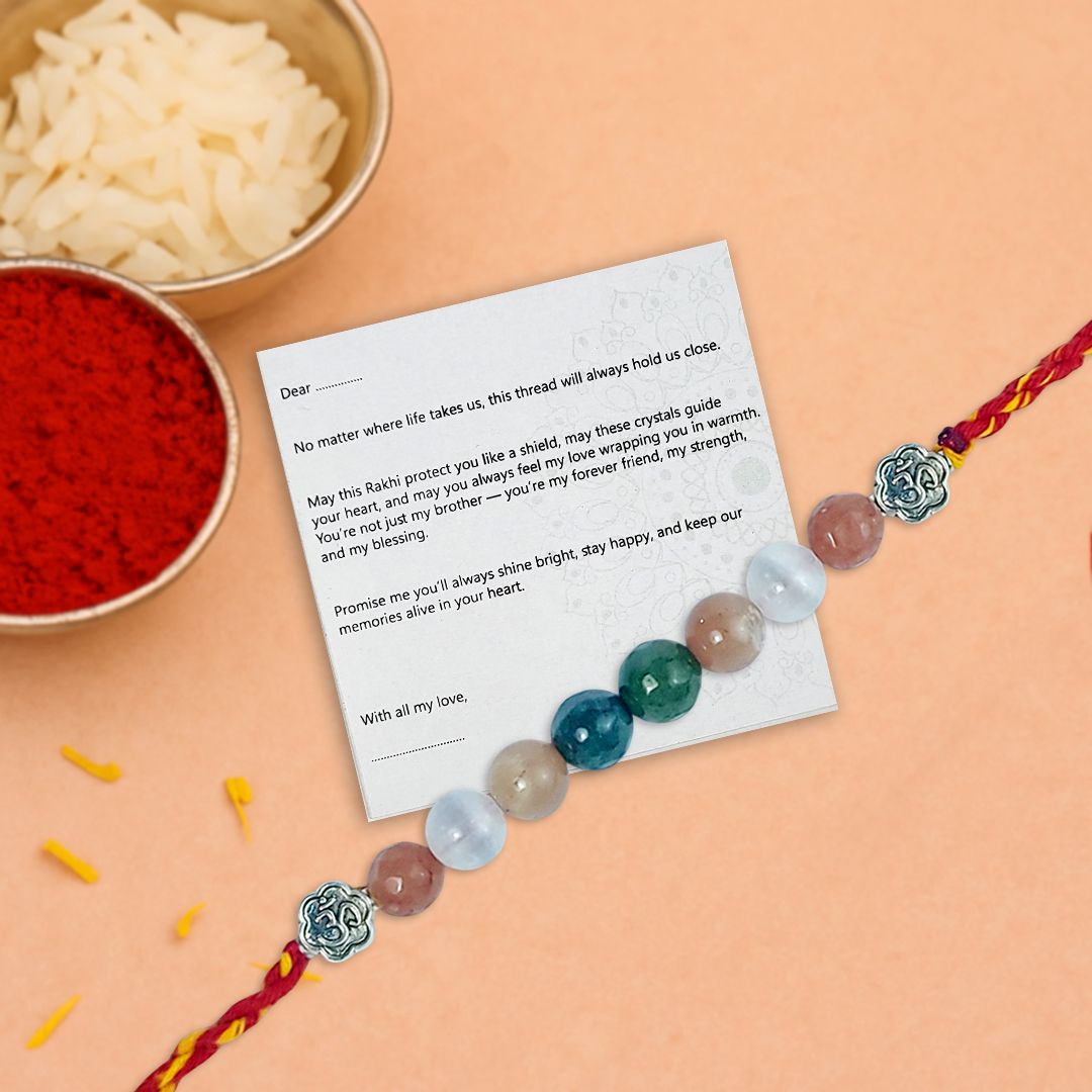 Crystal rakhi with a letter on a peach background, surrounded by traditional items.