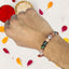Hand wearing a beaded rakhi with colorful petals on a white background