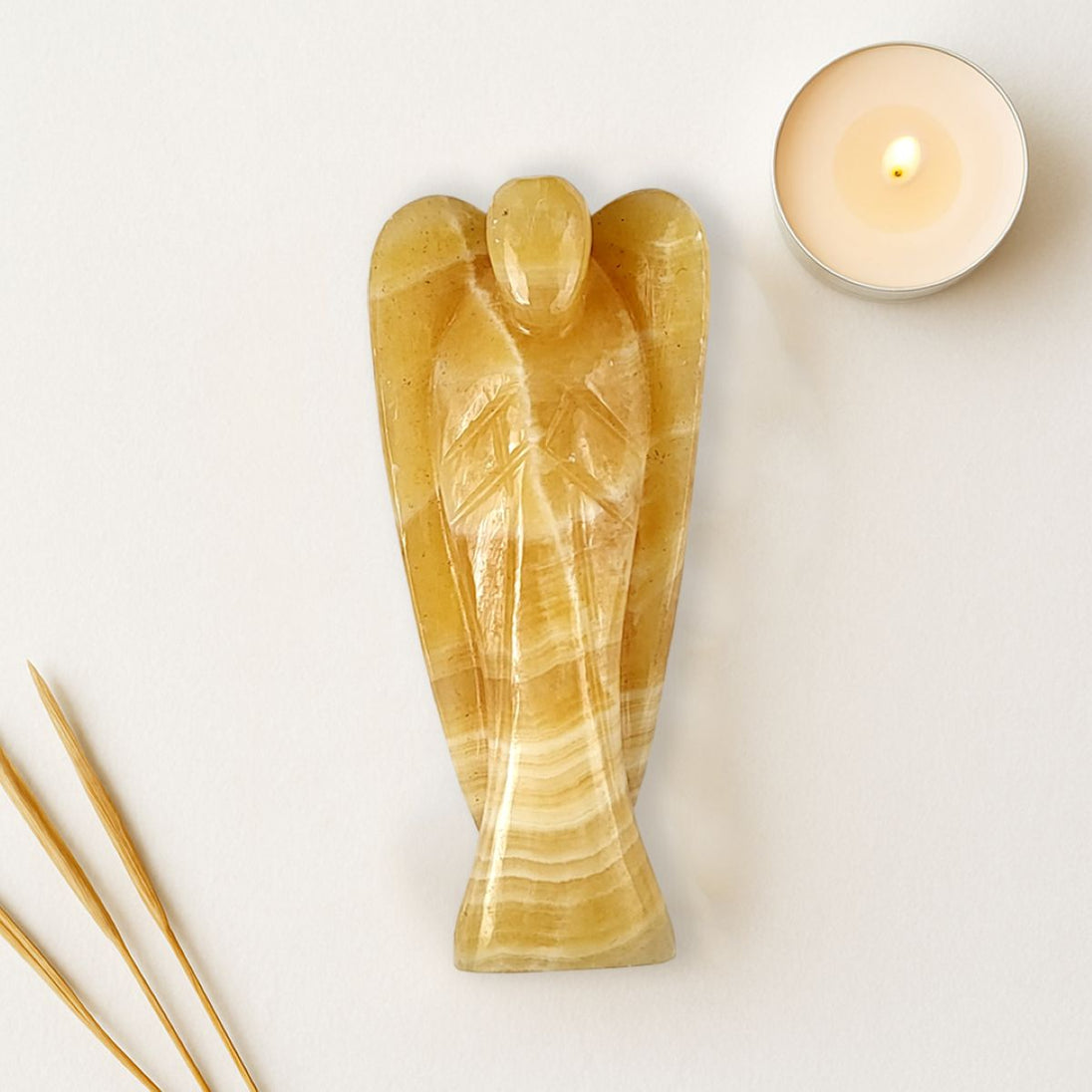 Decorative angel sculpture made of a golden stone material on a light background with a candle and incense sticks.