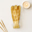 Decorative angel sculpture made of a golden stone material on a light background with a candle and incense sticks.