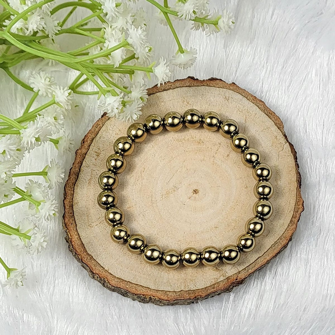 Gold beaded bracelet on a wooden slice with white flowers in the background