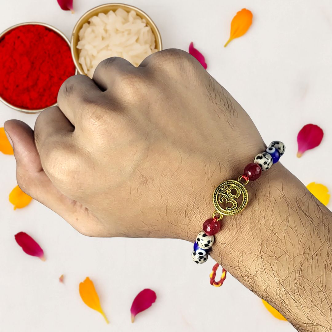 Hand wearing a beaded rakhi with a decorative charm, surrounded by colorful petals on a white background.