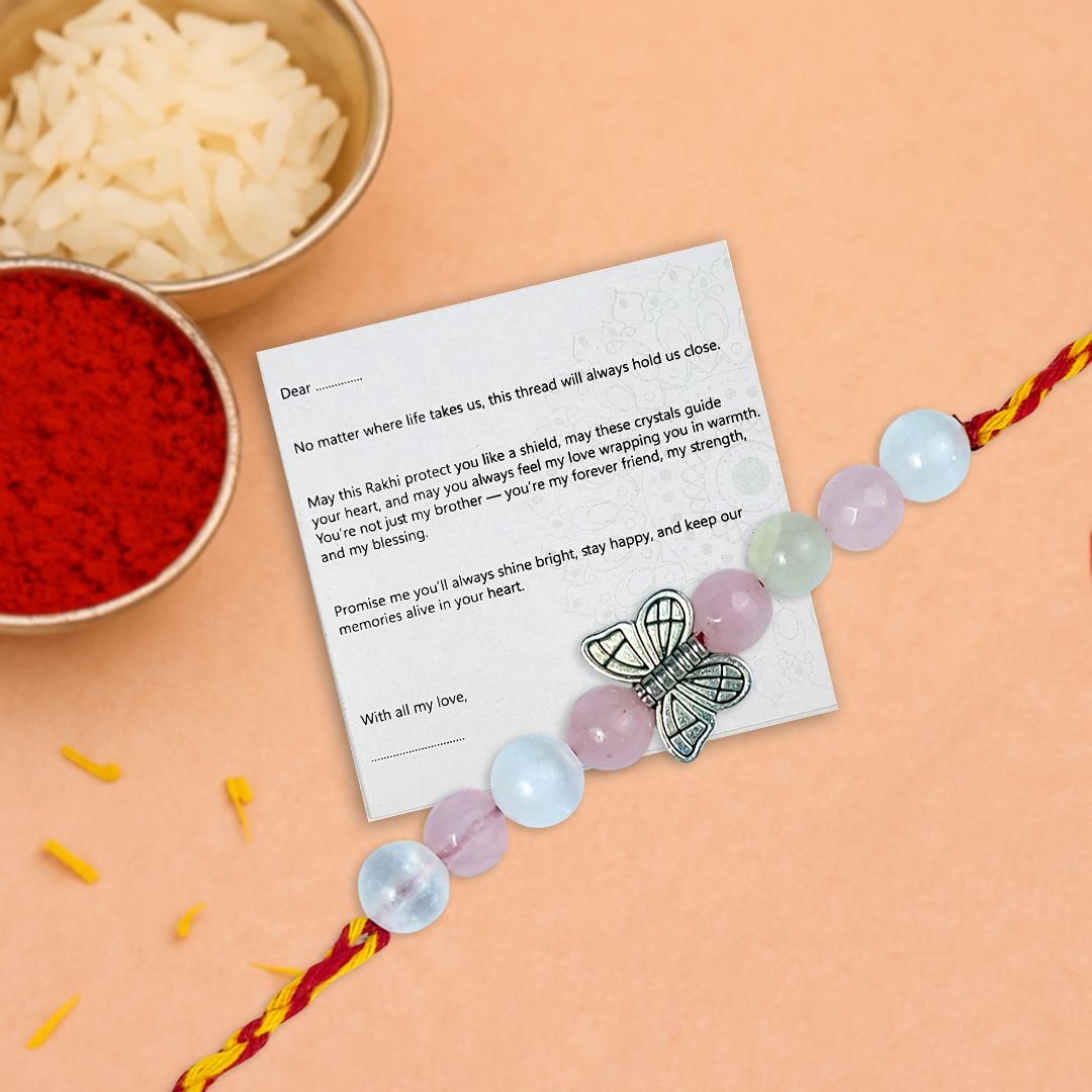 Beaded rakhi with a butterfly charm on a card, surrounded by bowls of red and white powder on an orange background.