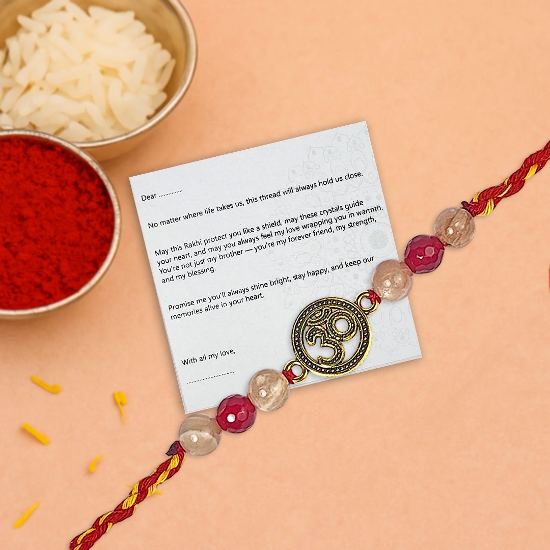 Decorative Rakhi with Om pendant on a card, surrounded by red powder and rice on a peach background