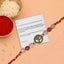 Decorative Rakhi with Om pendant on a card, surrounded by red powder and rice on a peach background