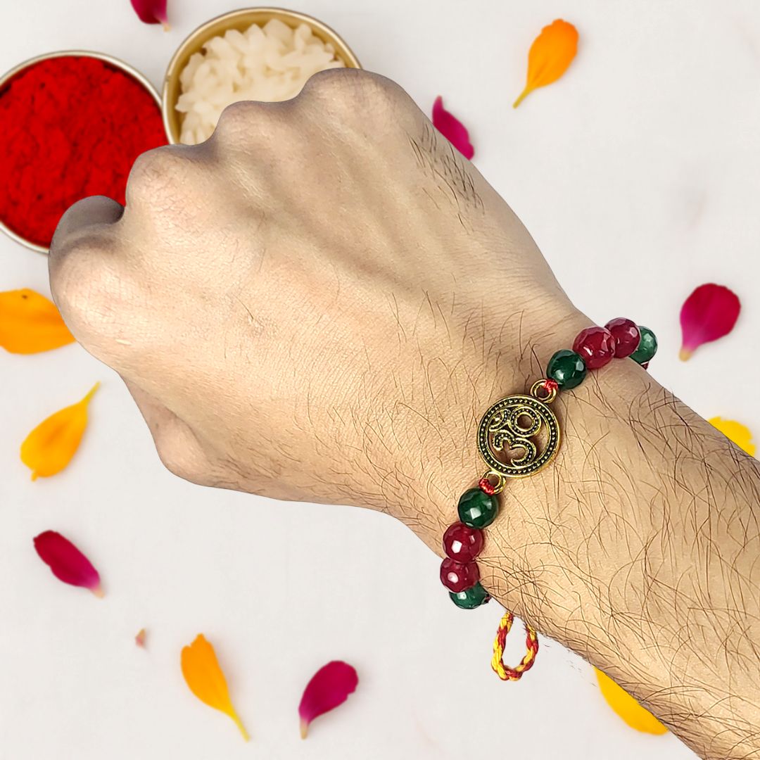 Hand wearing a beaded rakhi with a decorative charm, surrounded by colorful petals on a light background.