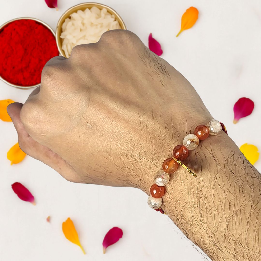 Hand wearing a beaded rakhi with red and white powders and petals in the background