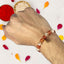 Hand wearing a beaded rakhi with red and white powders and petals in the background