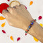 Hand wearing a beaded rakhi with colorful petals on a white background
