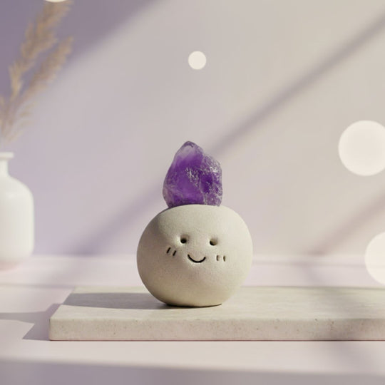 Ceramic smiley face object with a amethyst purple crystal on top against a soft, blurred background