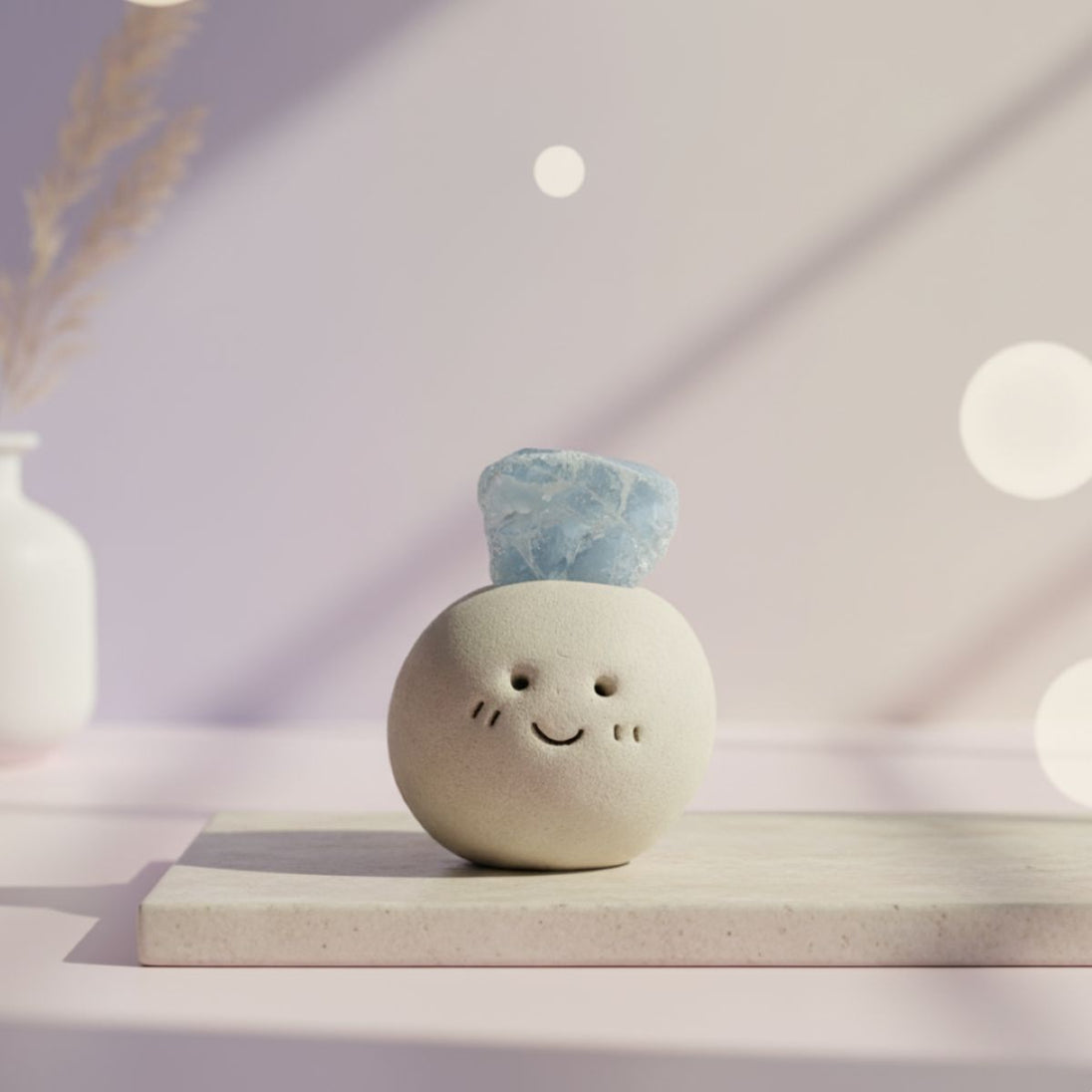Ceramic round ball with a smiling face and blue aquamarine crystal on top placed on a white surface with soft lighting