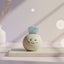 Ceramic round ball with a smiling face and blue aquamarine crystal on top placed on a white surface with soft lighting