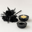 Black decorative roses and two black candle holders with a lit candle on a white background
