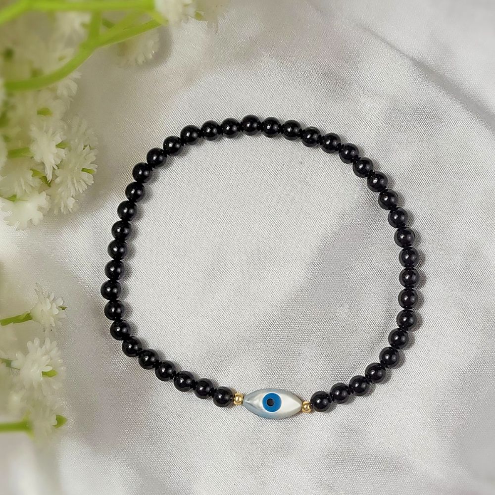 Black beaded bracelet with a blue evil eye charm on a white fabric background