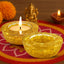 Two yellow crystal candle holders with lit candles on a decorative mat with a statue and marigold flowers in the background.
