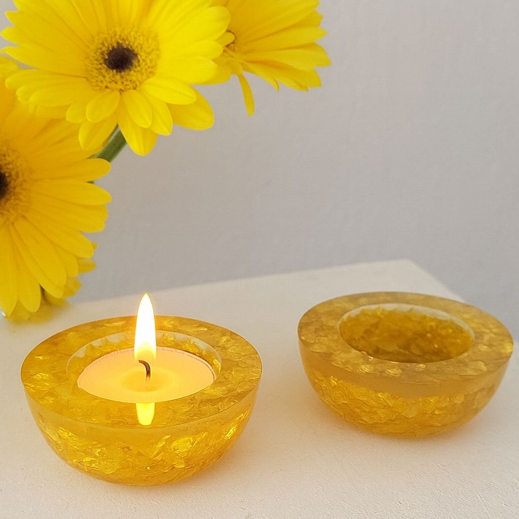 Two yellow candle holders with a lit candle and yellow flowers on a white surface