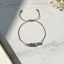 Gold thread bracelet with purple and green beads on a marble surface