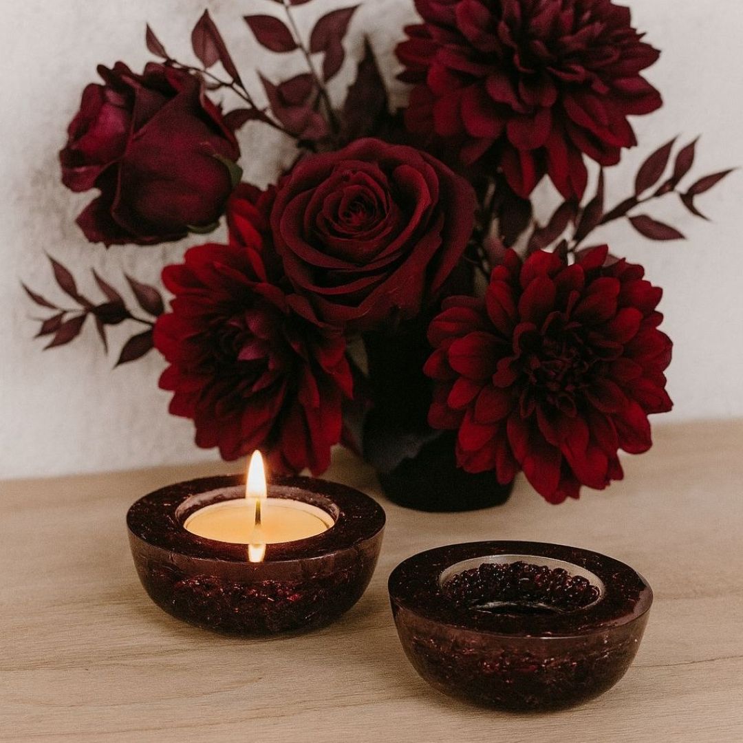 Two lit candles in dark holders with a bouquet of red flowers on a wooden surface.