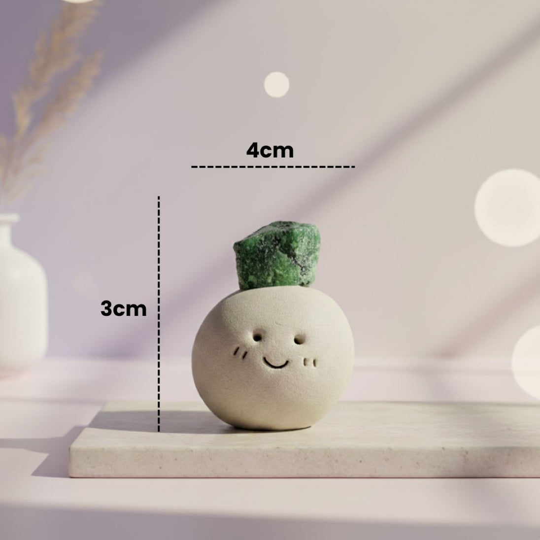 Small decorative item with a smiley face and green crystal on top, placed on a light surface with measurement labels.