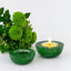 Two green candle holders with a lit candle and a bouquet of green flowers on a white background