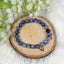 Blue beaded lapis lazuli bracelet with a gold accent on a wooden slice with white flowers in the background