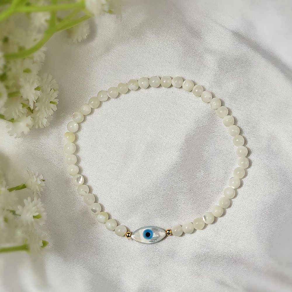 white beaded bracelet with an evil eye charm on a white fabric background