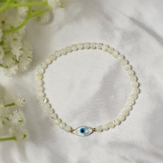 white beaded bracelet with an evil eye charm on a white fabric background