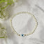 white beaded bracelet with an evil eye charm on a white fabric background