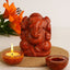 Red jasper stone Ganesh statue with a lit candle in tea light holder and orange flowers on a white background