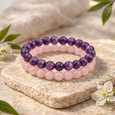 Amethyst and rose quartz bead bracelets stacked on a stone slab with white flowers