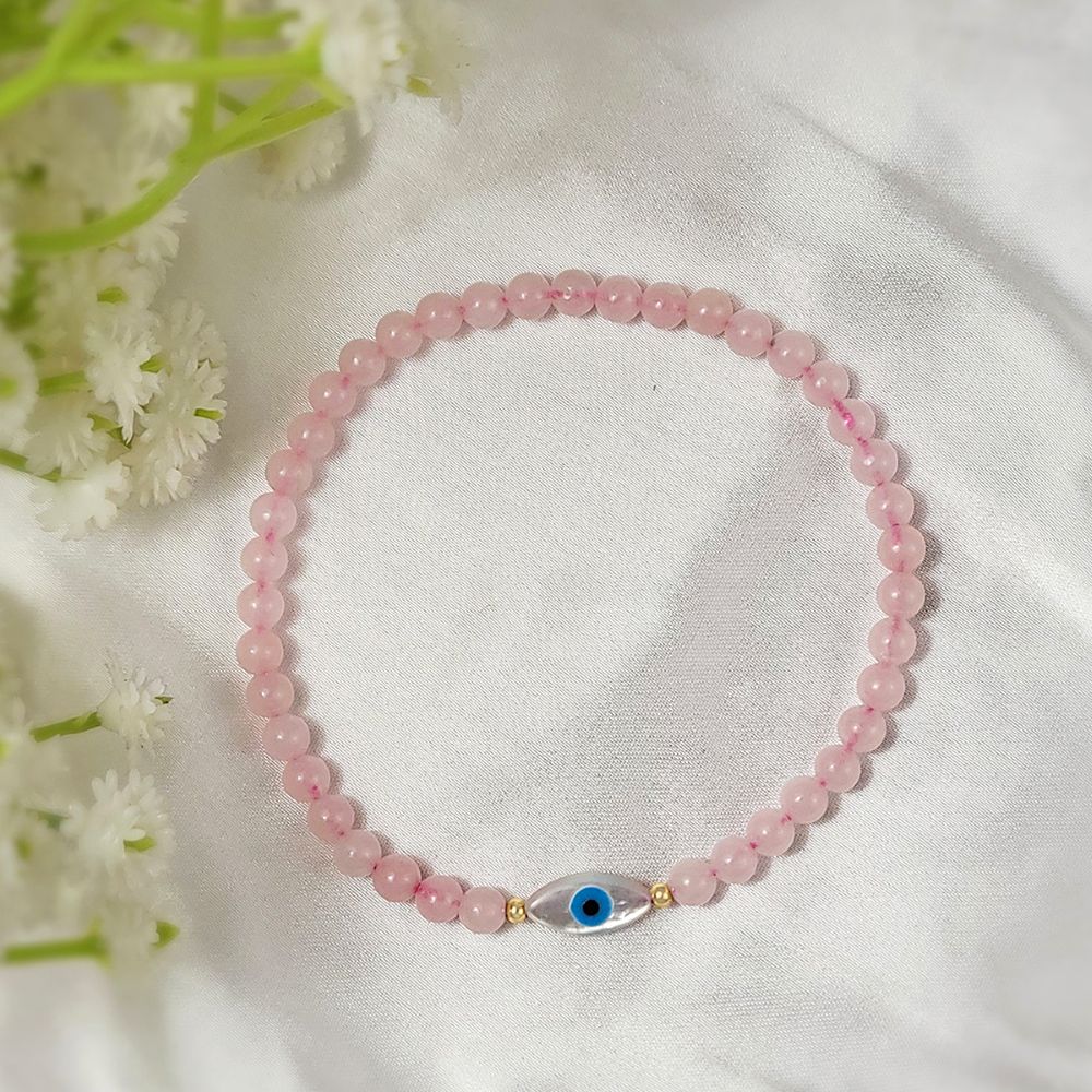 Pink beaded bracelet with a blue evil eye charm on a white fabric background with flowers.