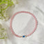 Pink beaded bracelet with a blue evil eye charm on a white fabric background with flowers.