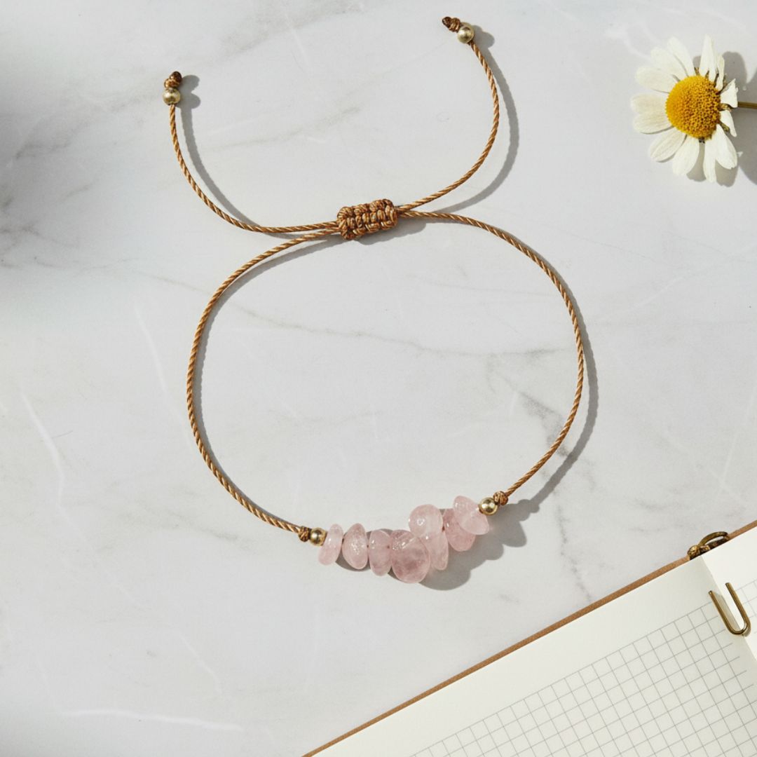 bracelet with pink stone beads and gold thread on a marble surface