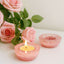 Pink candle holder with a lit candle and pink roses on a light background