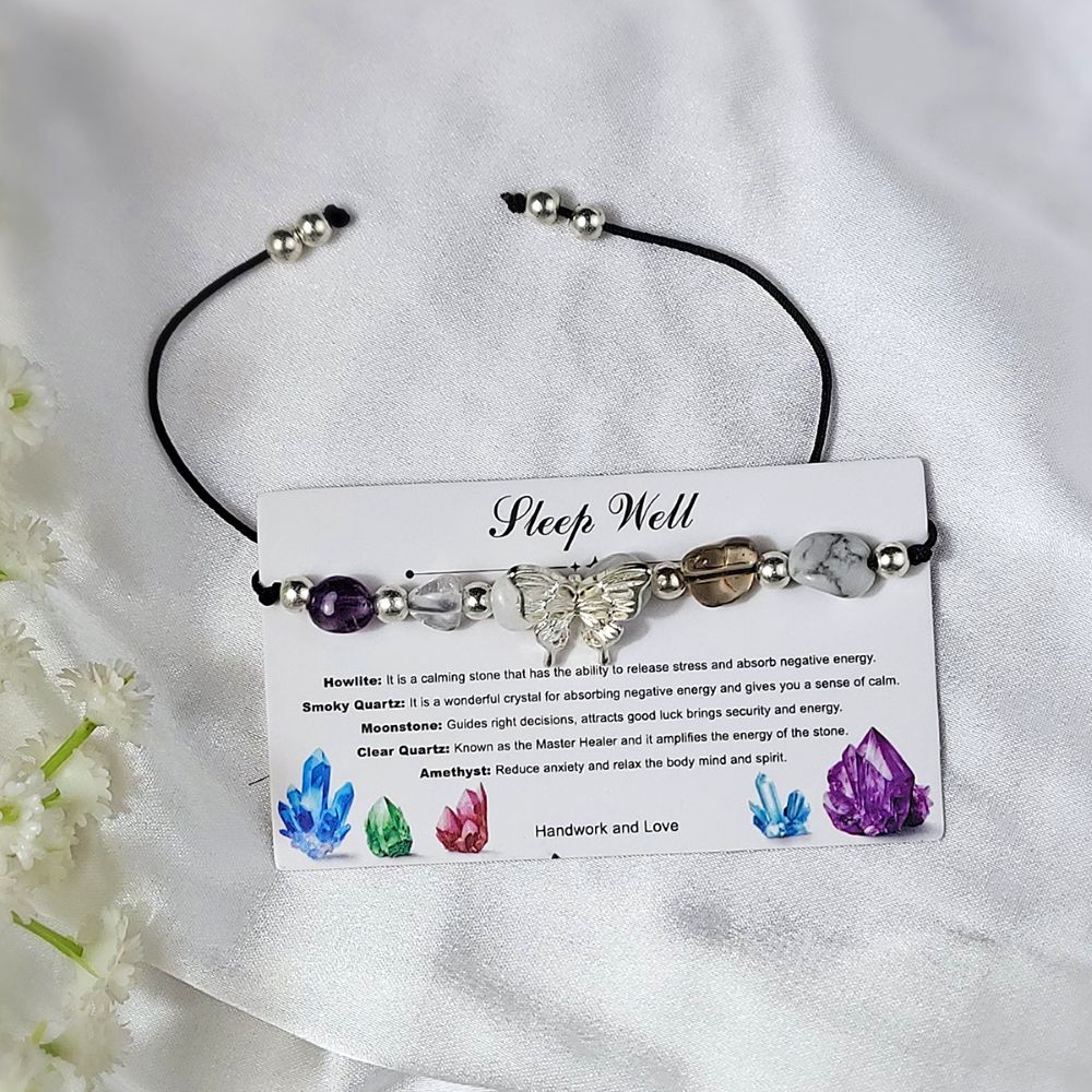 Crystal bracelet with stones on a card explaining their properties, on a white fabric background with flowers.