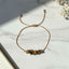 golden thread bracelet with tiger eye stone beads on a light marble surface with flowers