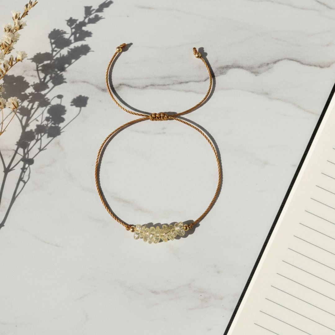 golden thread bracelet with yellow quartz beads placed on a marble surface with a notebook and dried flowers.