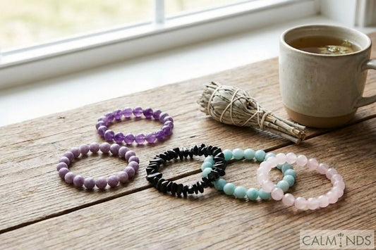 Collection of healing crystal bracelets for anxiety, including Amethyst, Lepidolite, Black Tourmaline, Amazonite, and Rose Quartz on a wooden table.