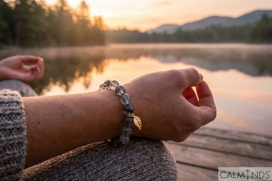 Woman meditating by a calm lake at sunrise wearing a Calminds Black Rutile Quartz bracelet on her left wrist for anxiety relief and grounding.