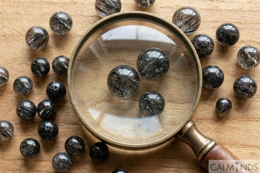 Genuine Black Rutile Quartz beads with magnifying glass on wooden table for inspection.