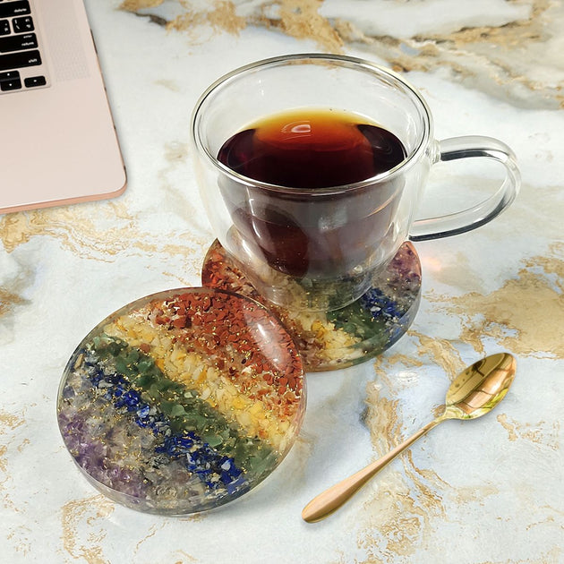Clear mug with dark liquid on a colorful coaster on a marble surface with a laptop.