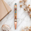 Decorative pen with chakra design on a marble surface with notebook and crystals.