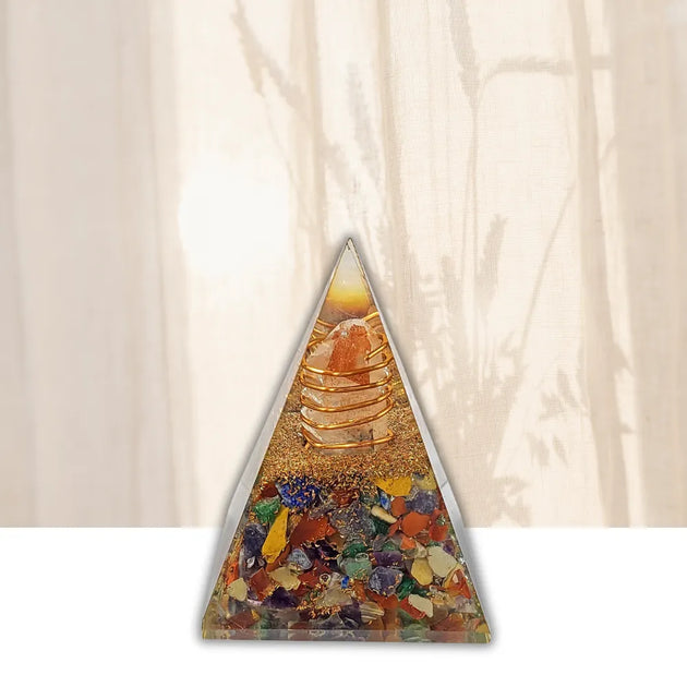 A triangular crystal tower ornament filled with multicolored gemstones and a gold-toned spiral structure, set against a warm cream background with soft shadow projections.