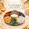 7 Chakra Tea Light Holder with a lit candle in its gold-tone centre, ringed by seven colour sections of natural crystal chips