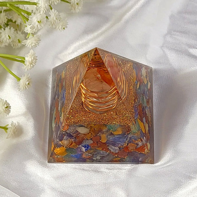 Decorative 7 chakra pyramid with colorful stones on a white fabric background with flowers.