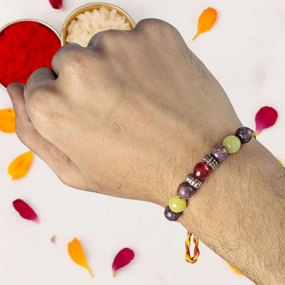 Hand wearing a colorful beaded rakhi with red and white powder in the background