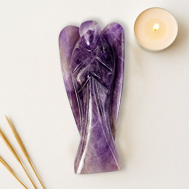 Purple crystal angel sculpture next to a candle on a light background